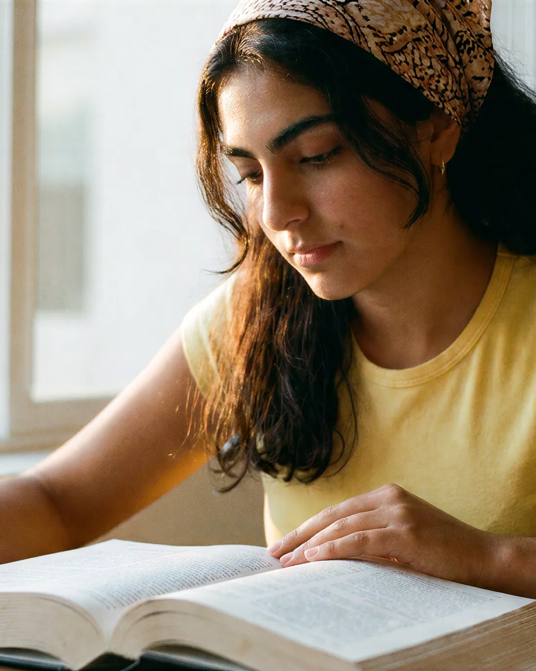 A student reading at a sunlit window.